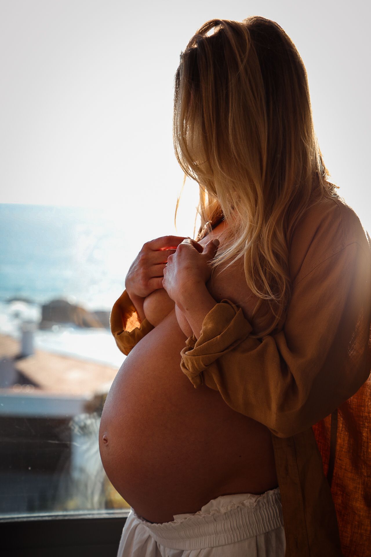 Pregnant woman holding belly with coastal sunset backdrop, Sydney maternity photography