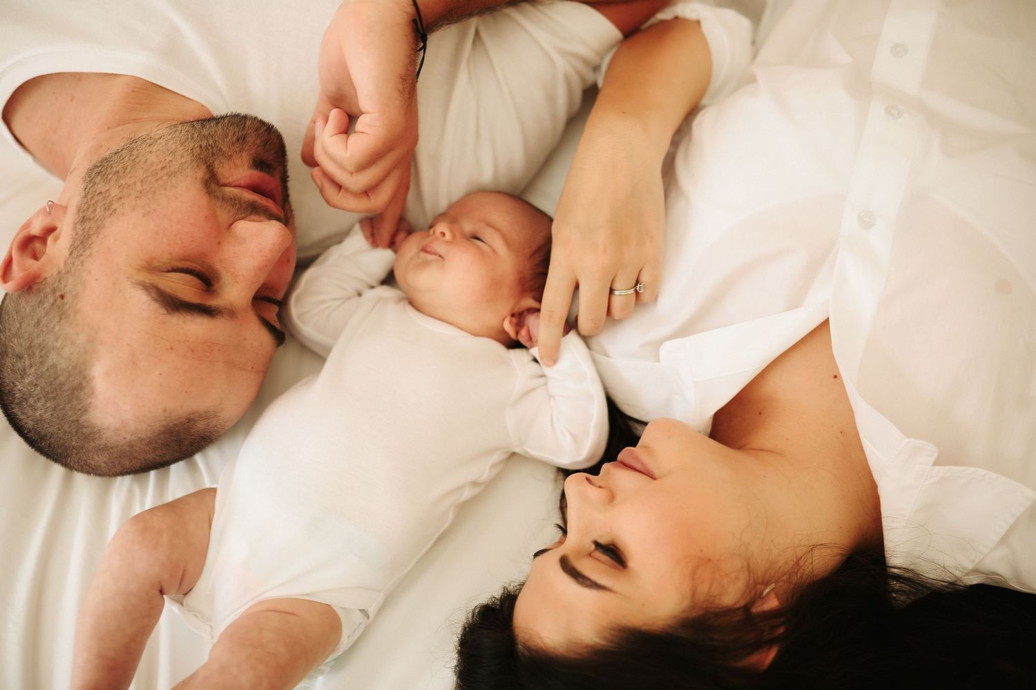 Parents lying with newborn baby between them in bed, in-home newborn photography Sydney