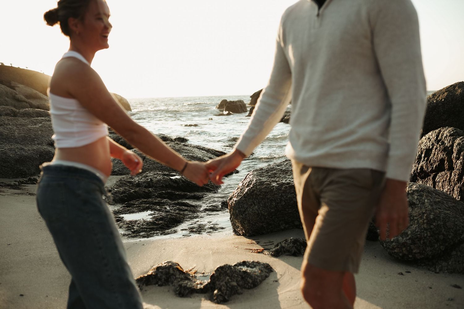 Pregnant couple holding hands walking along rocky beach, Sydney maternity photography session