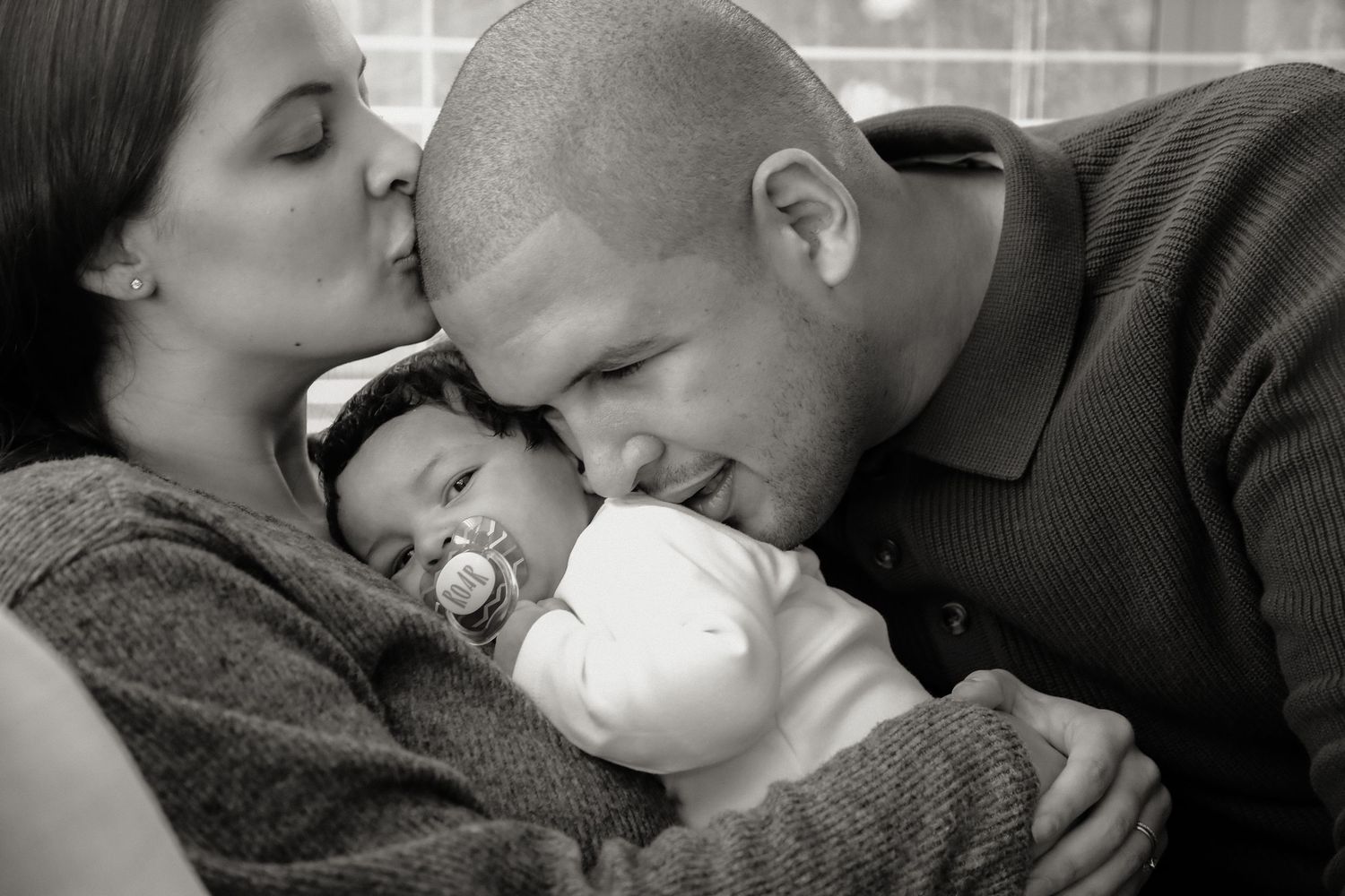 Black and white portrait of father kissing baby held by mother, Sydney family photography