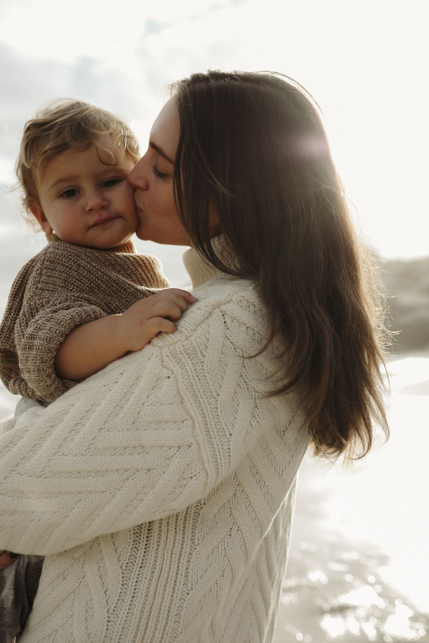 Mother kissing toddler's cheek in cosy knitwear by the coast, Sydney family photographer