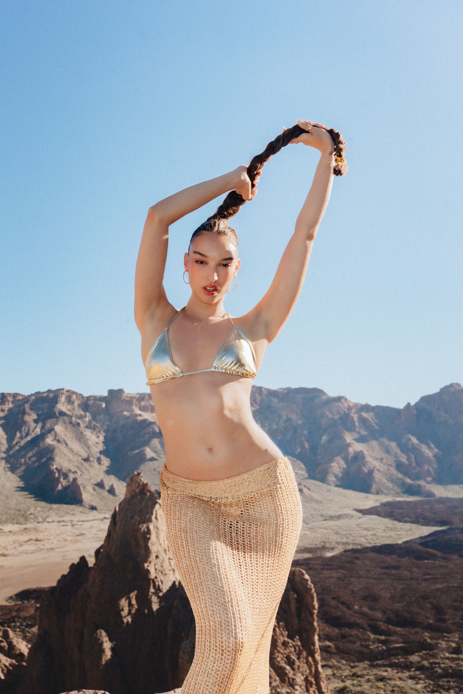 Fashion portrait of a model in a gold bikini and crochet skirt against volcanic mountains, from Anya MacLaren's Tenerife photography