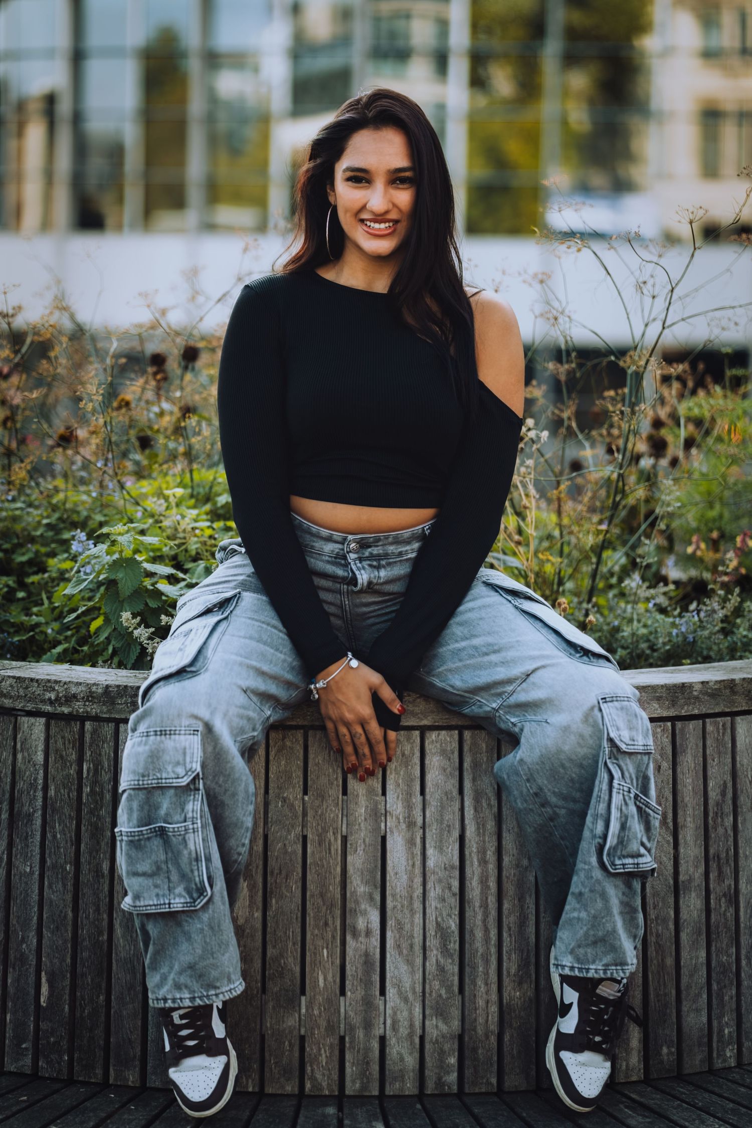 Portrait of a woman in cargo jeans and a black top sitting on a garden bench, by Anya MacLaren Photography