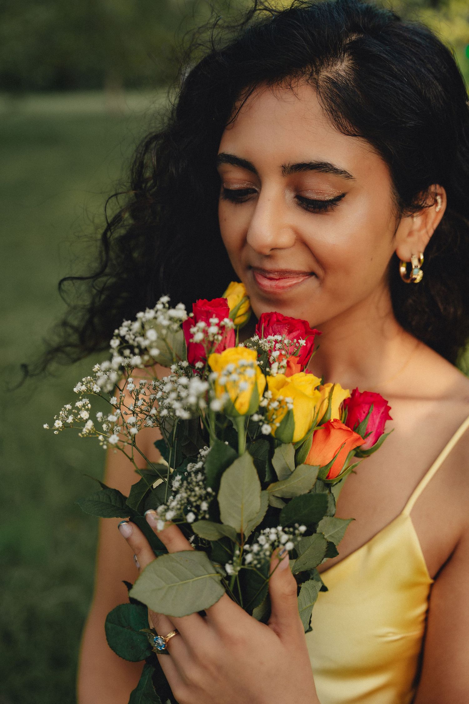 Engagement portrait of a bride-to-be smelling a bouquet of red and yellow roses, by Anya MacLaren Photography