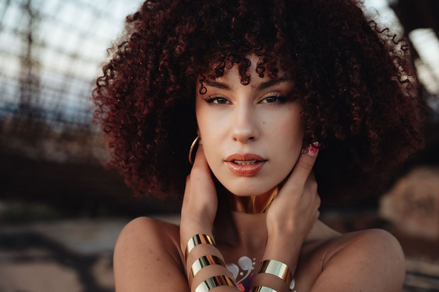 Close-up beauty portrait of a model with curly red hair and gold jewellery in warm evening light, by Anya MacLaren Photography