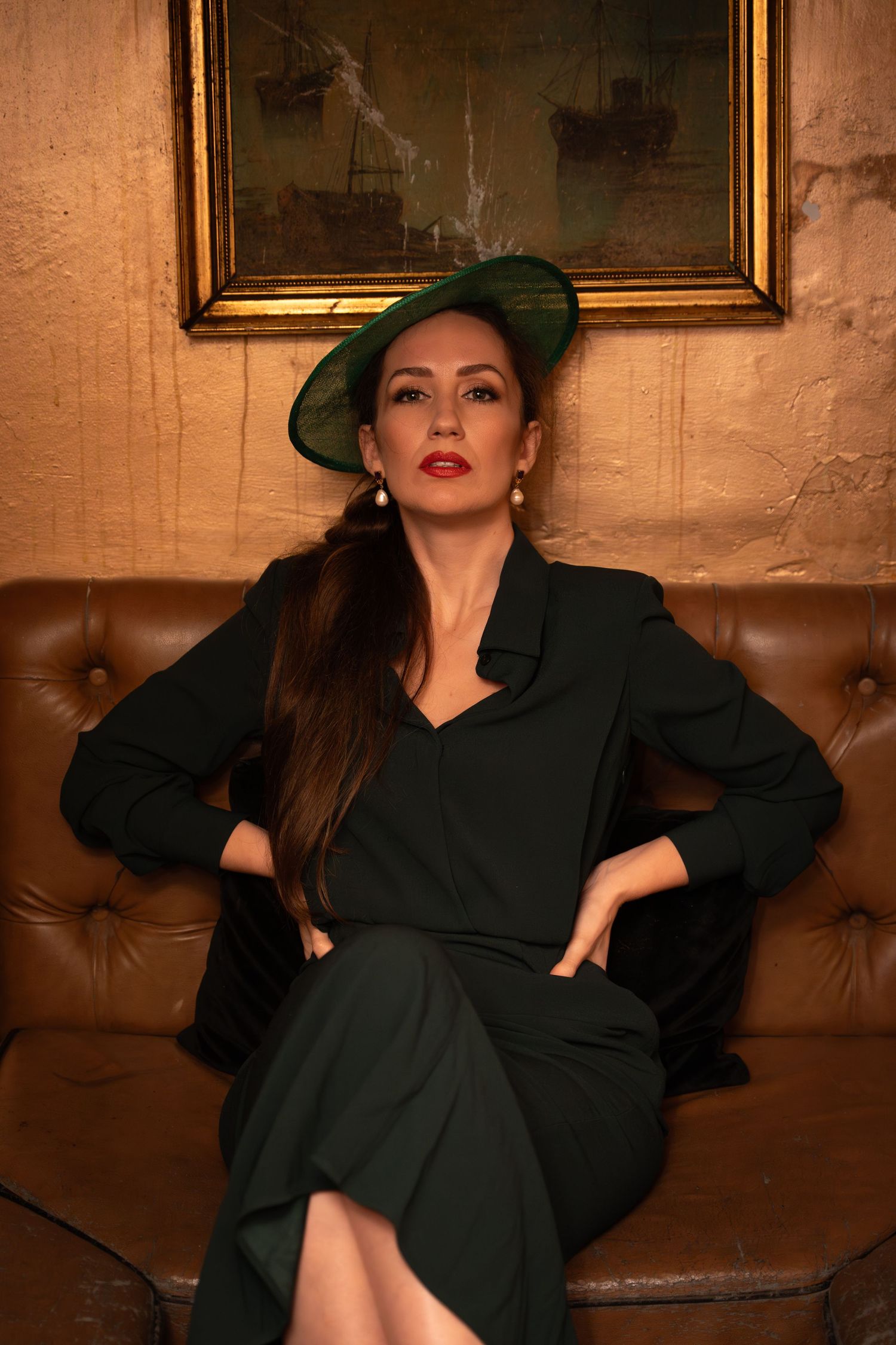 Vintage-style portrait of a woman in a dark green dress and hat on a leather sofa, by Anya MacLaren Photography