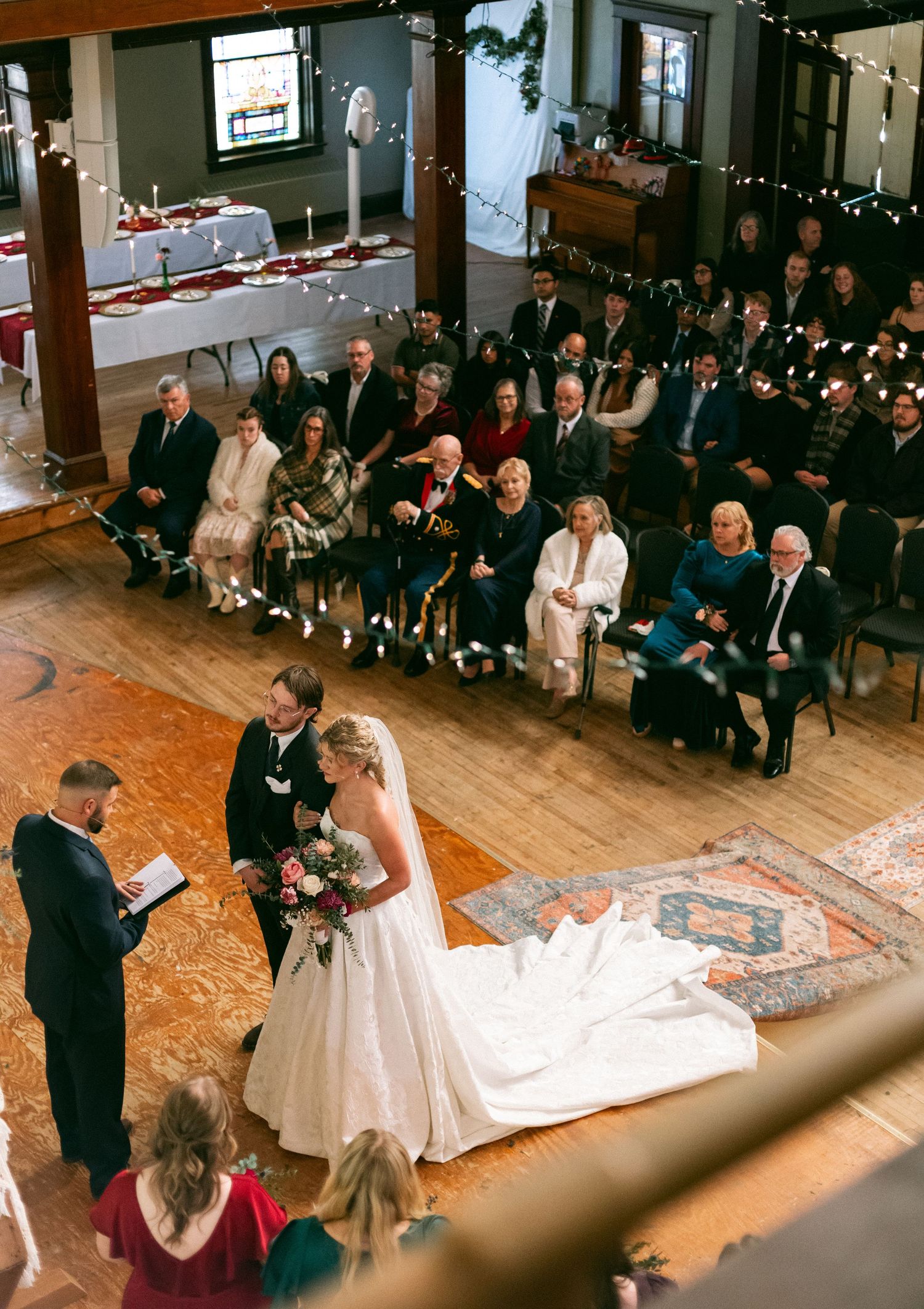Aerial view of a wedding ceremony in a rustic venue with guests seated on both sides as couple stands before officiant.