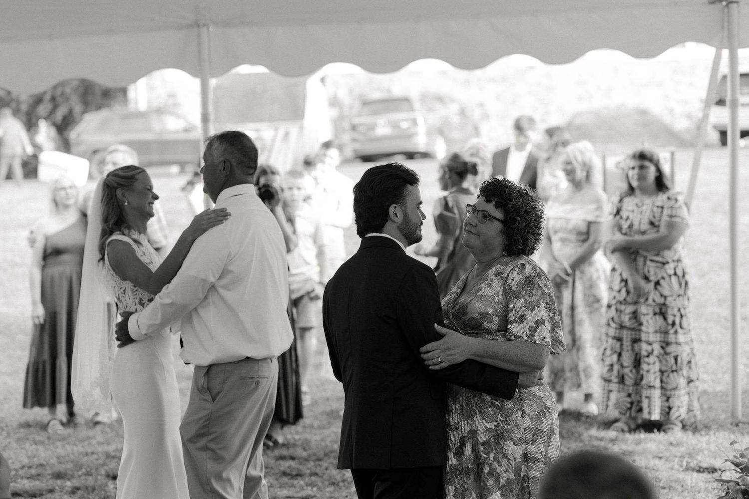 Black and white photo of couples dancing at an outdoor wedding reception under a white tent.