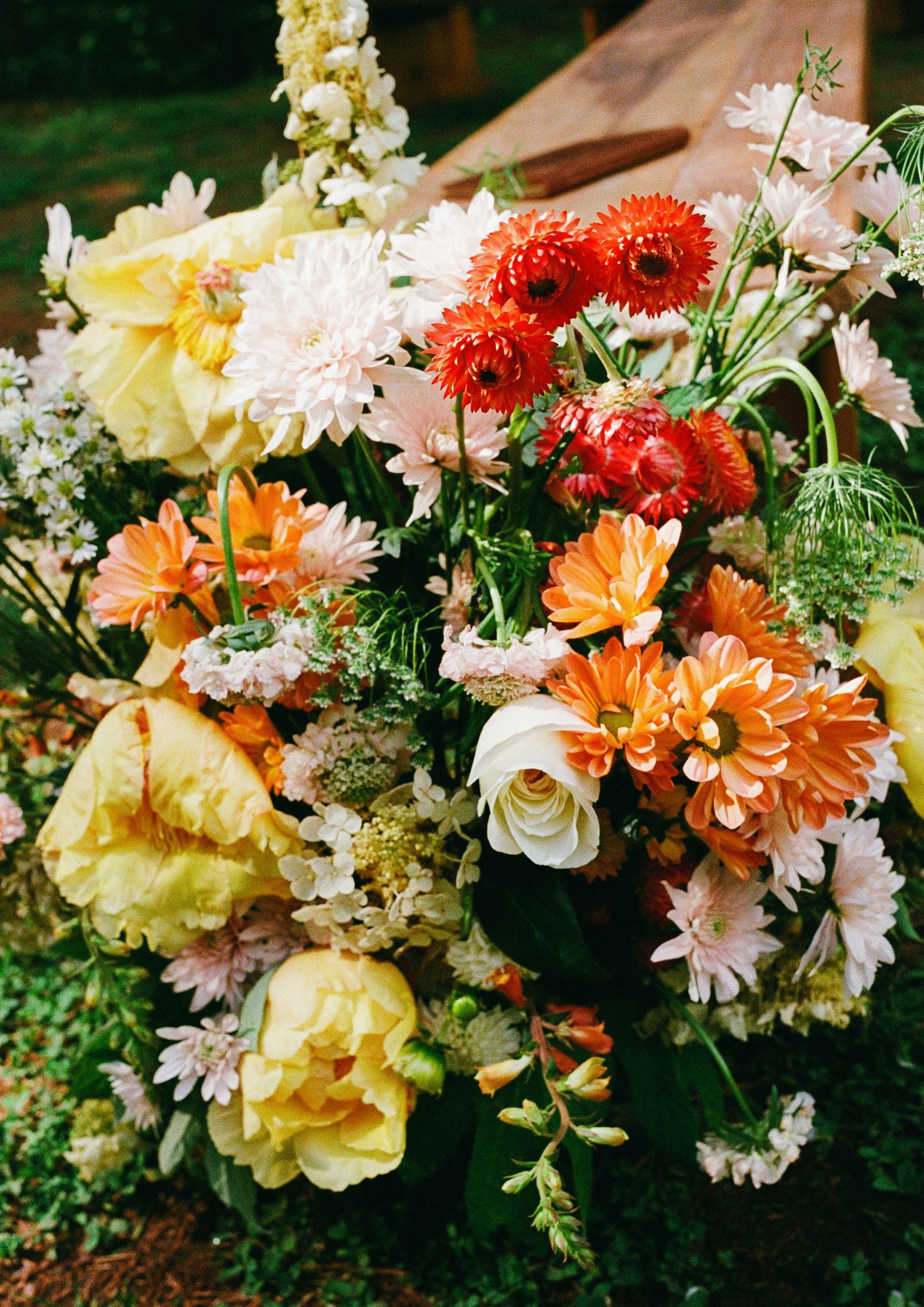 Lush floral arrangement featuring orange gerberas, yellow dahlias, white roses, and red chrysanthemums in a vibrant bouquet.