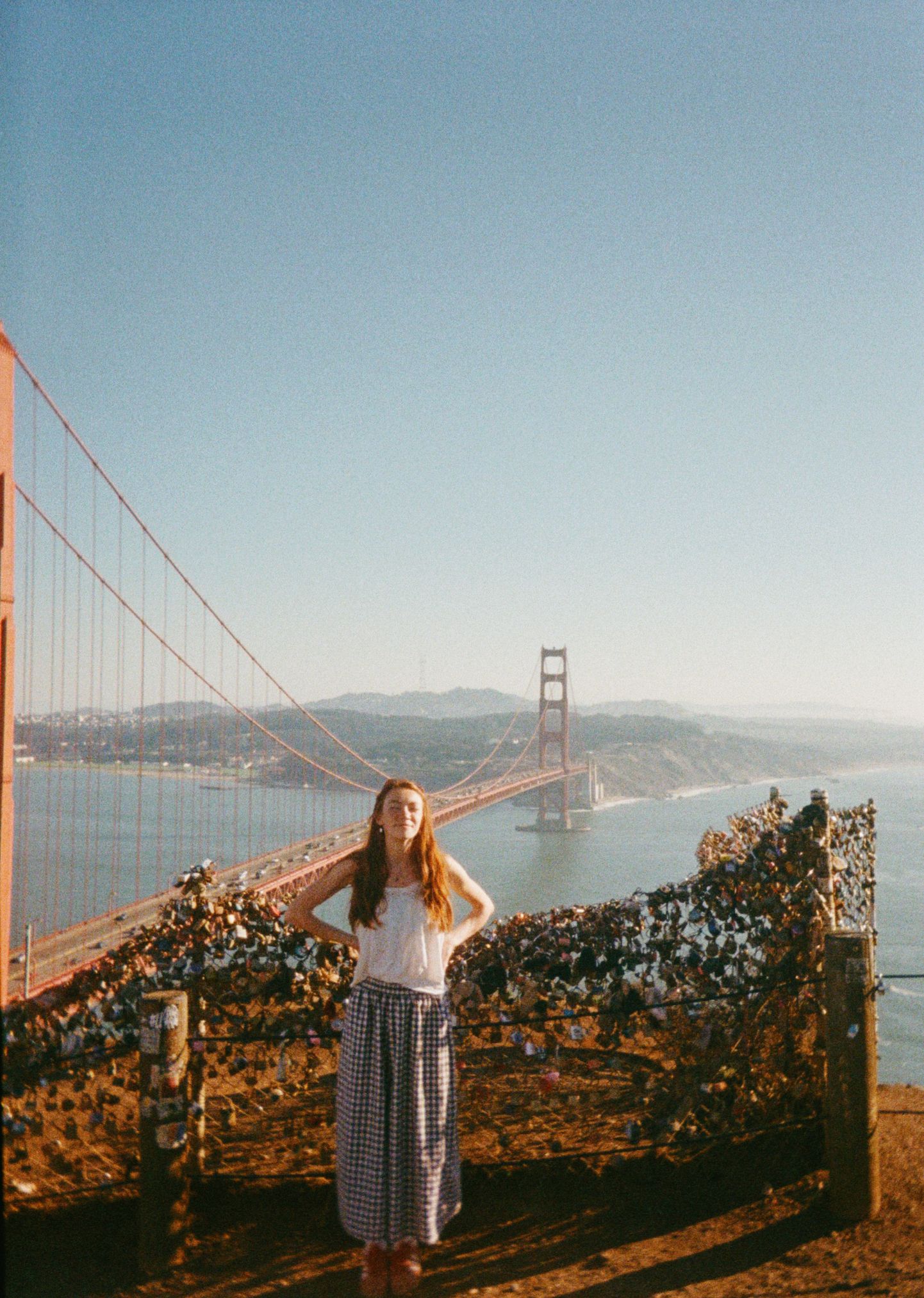 Woman in white top and plaid skirt poses near the Golden Gate Bridge in San Francisco on a clear sunny day.