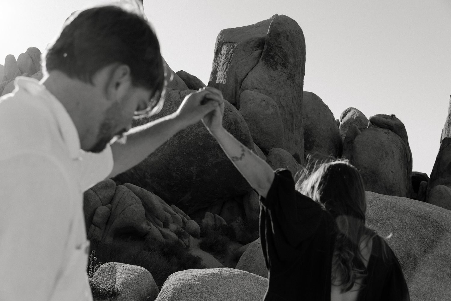 Black and white photo of a couple holding hands among large boulders in an outdoor setting.