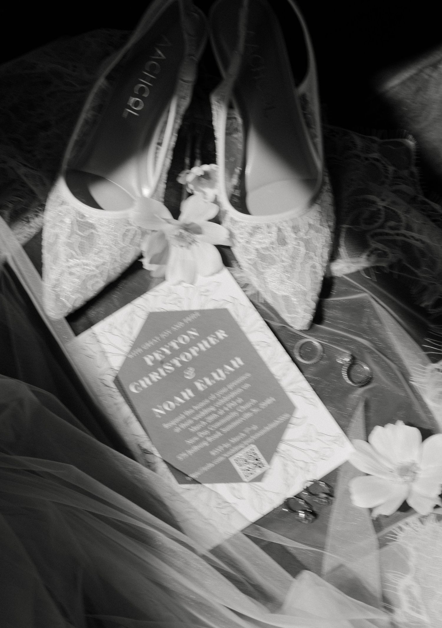 Black and white wedding flat lay with lace bridal shoes, invitation for Peyton Christopher and Noah Elijah, rings, and flowers.