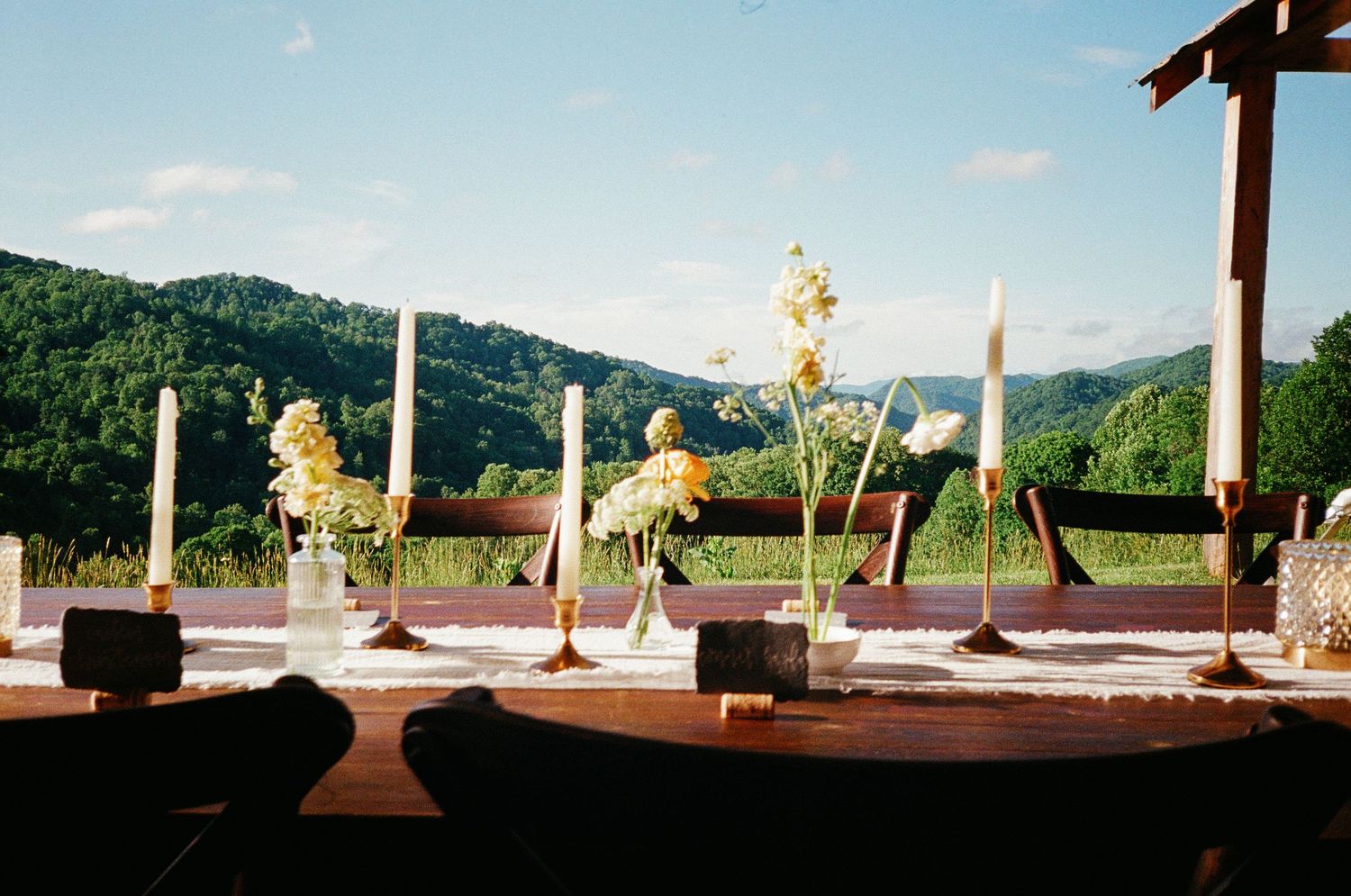 Elegant outdoor wedding table with yellow floral arrangements and candles, overlooking lush green mountain valley.