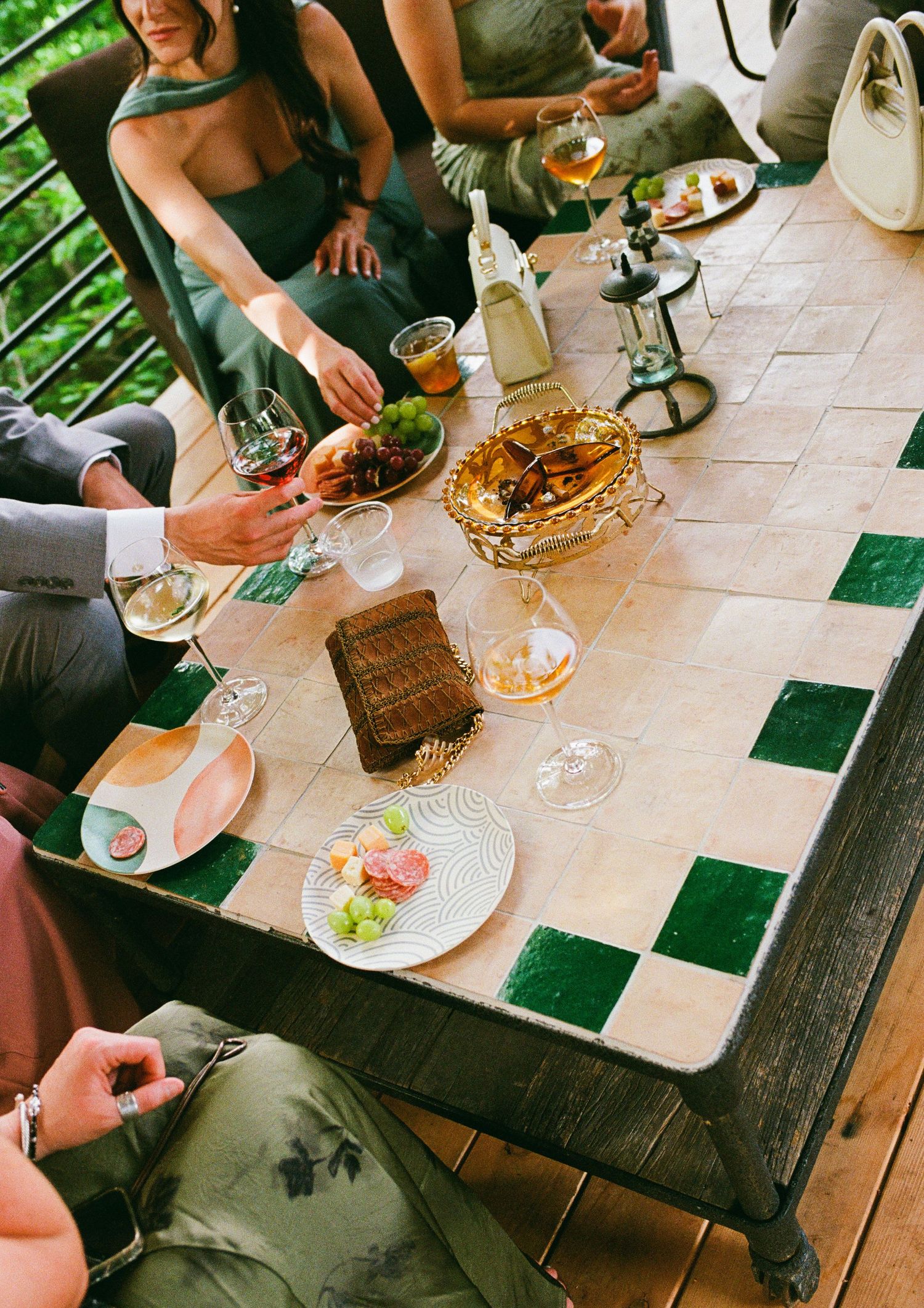 Guests gather around a mosaic tile table with wine, appetizers, and elegant dishware at an outdoor dinner party.