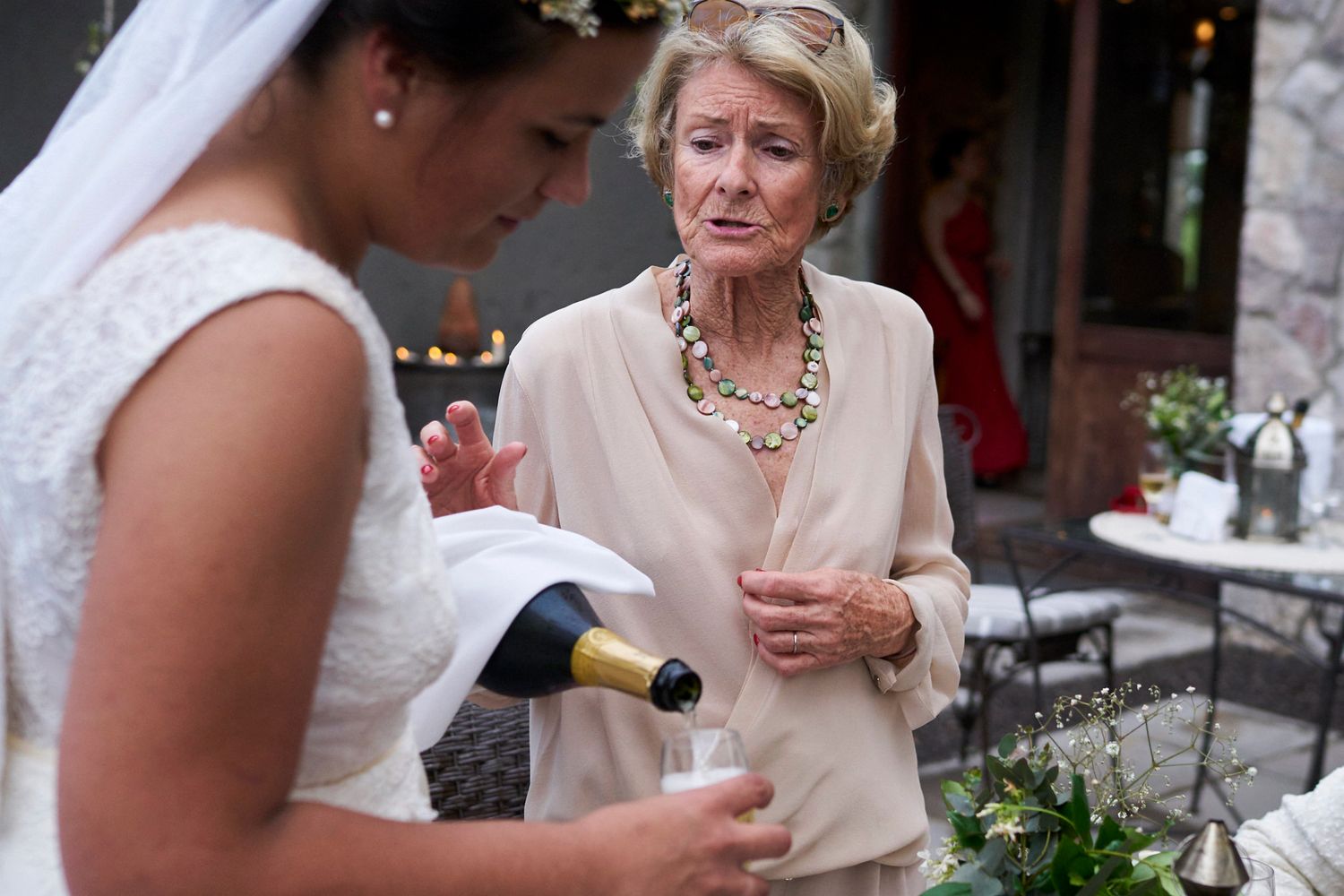 Abuela pidiéndole que no beba demasiado a la Novia que se está sirviendo champán durante la recepción al aire libre