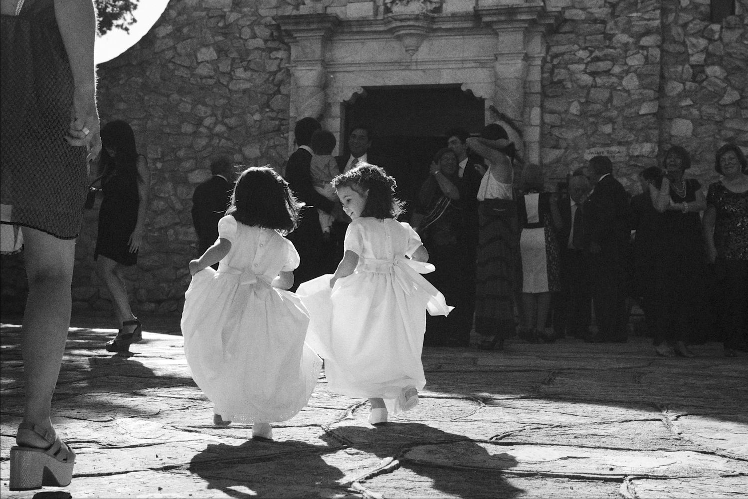 Foto en blanco y negro de dos niñas con vestidos blancos corriendo hacia la entrada de una iglesia de piedra