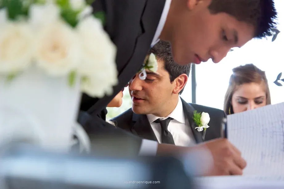 Novio a punto de besar a la novia mientras otro hombre firma como testigo