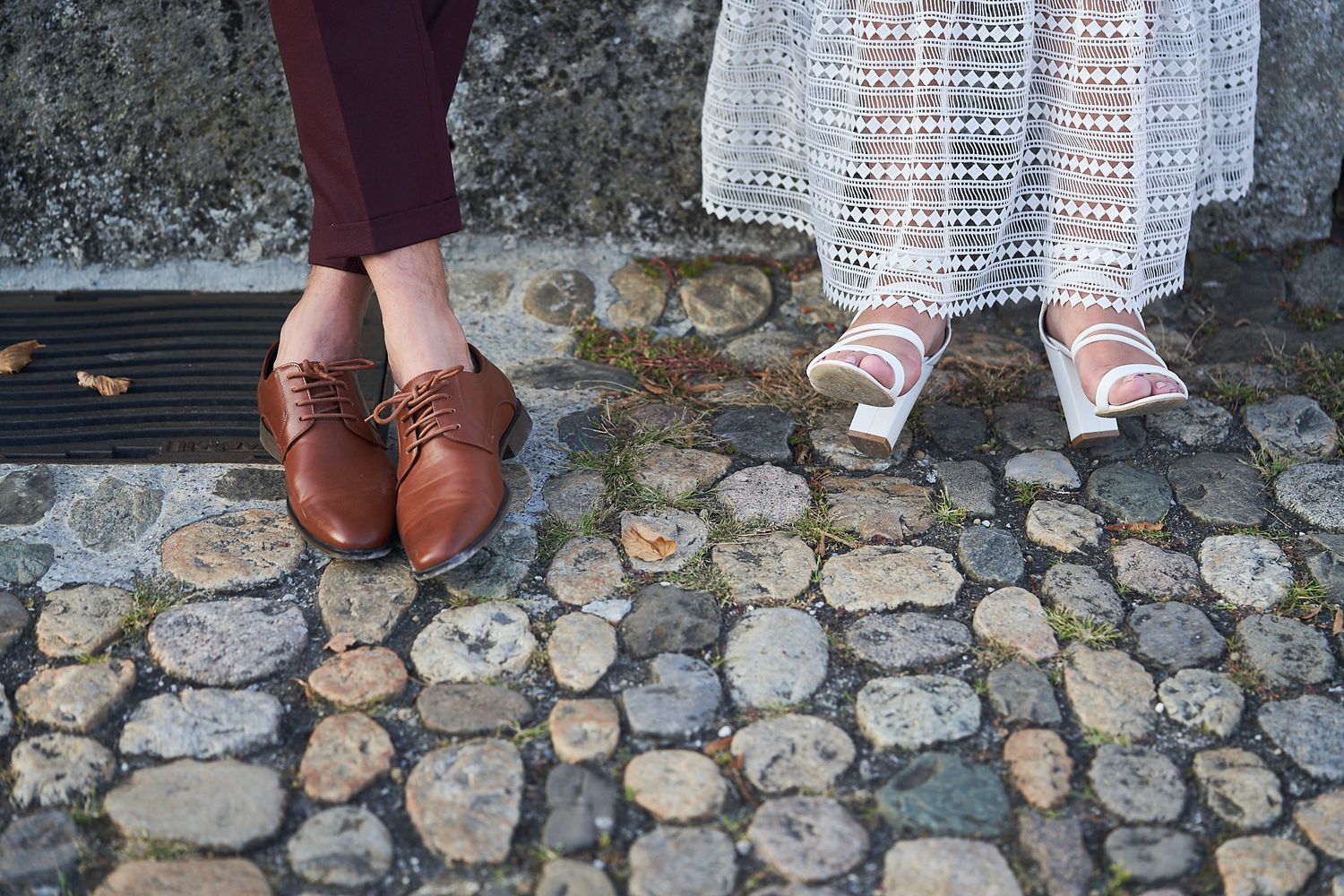 Primer plano de los zapatos de los novios, marrones y blancos, sobre un piso de adoquines