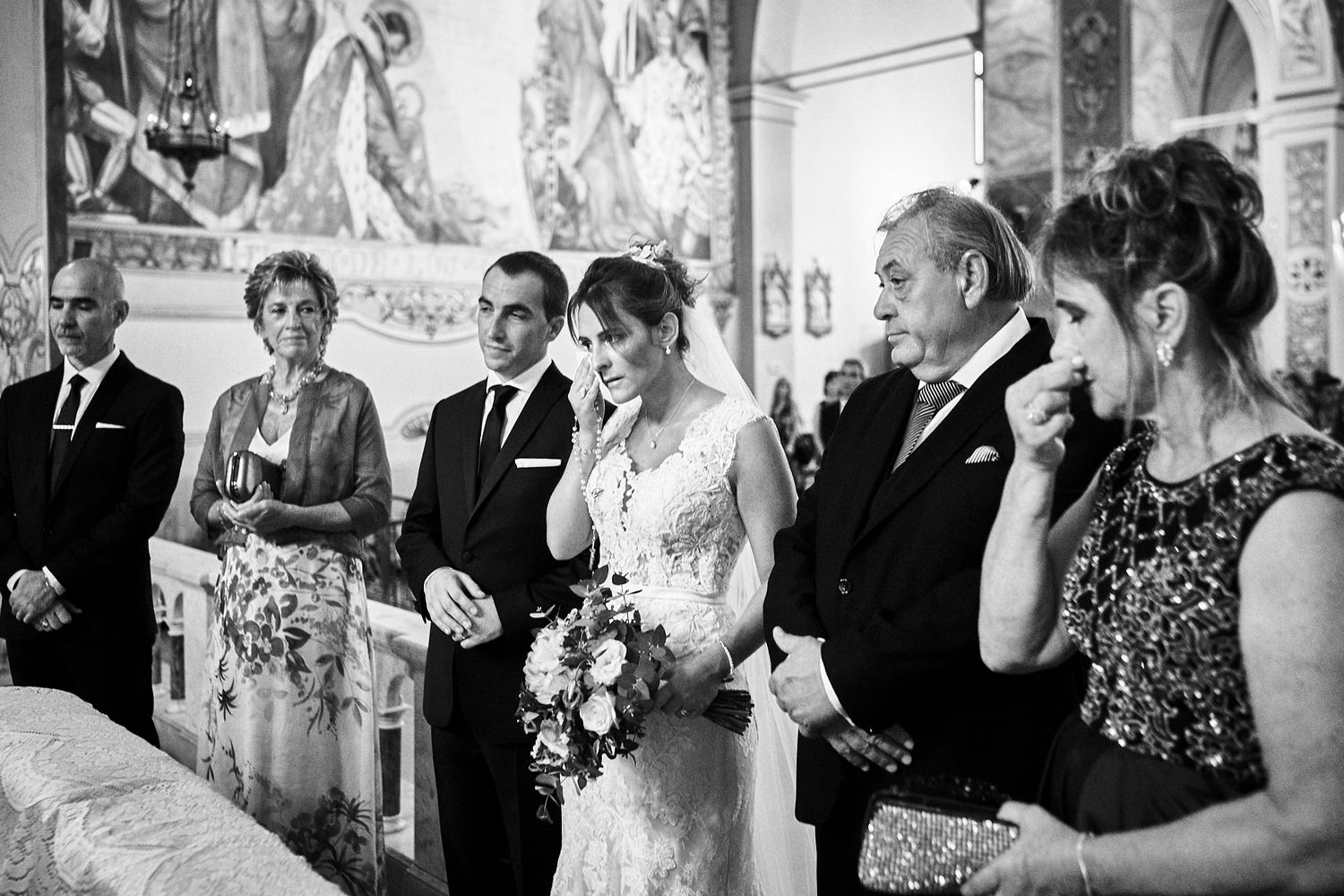 Foto en blanco y negro de la novia emocionada junto al novio y su padre durante la ceremonia religiosa