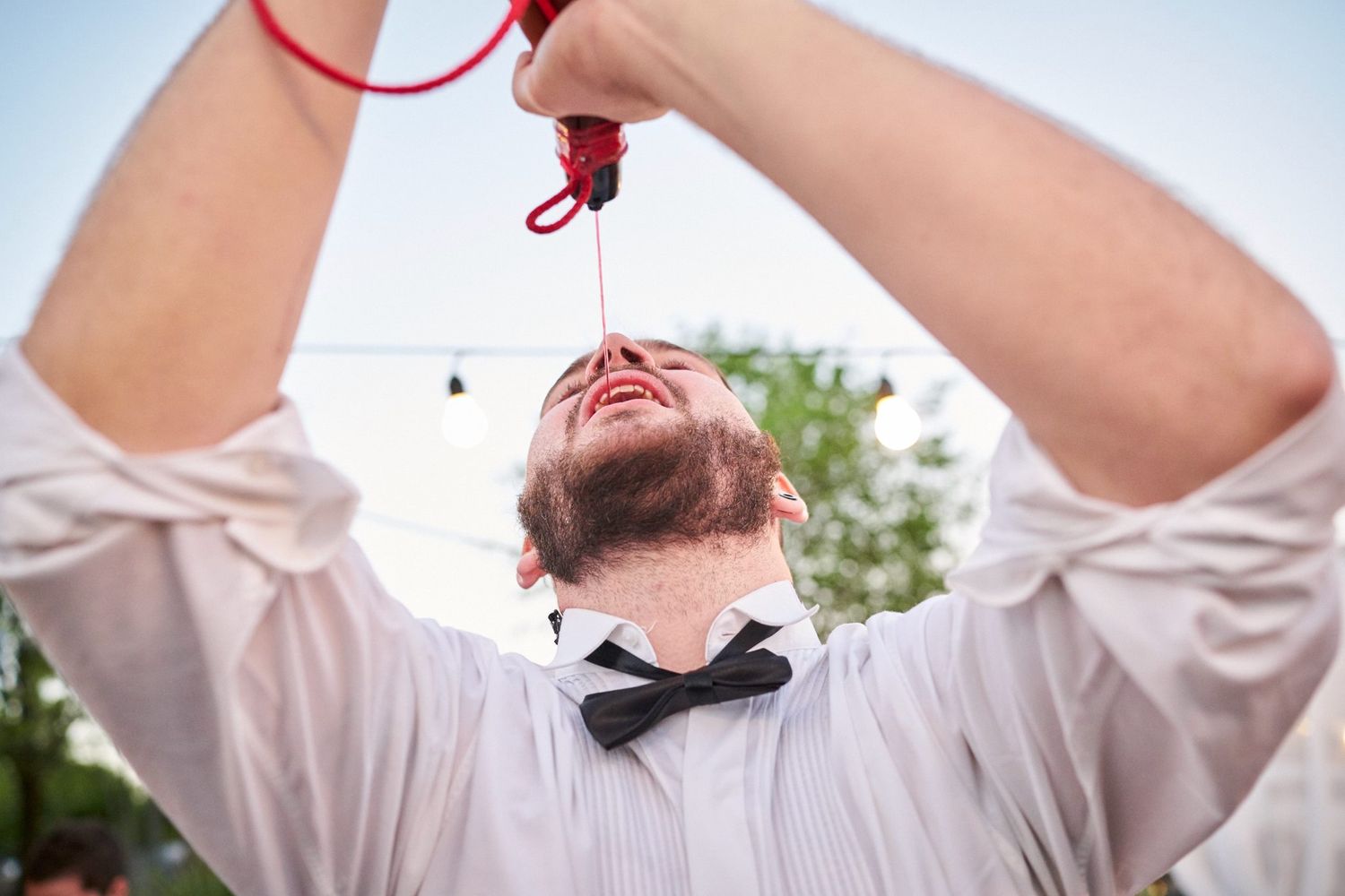Invitado con moño levantando la cabeza mientras sostiene una bota de vino, bajo luces colgantes