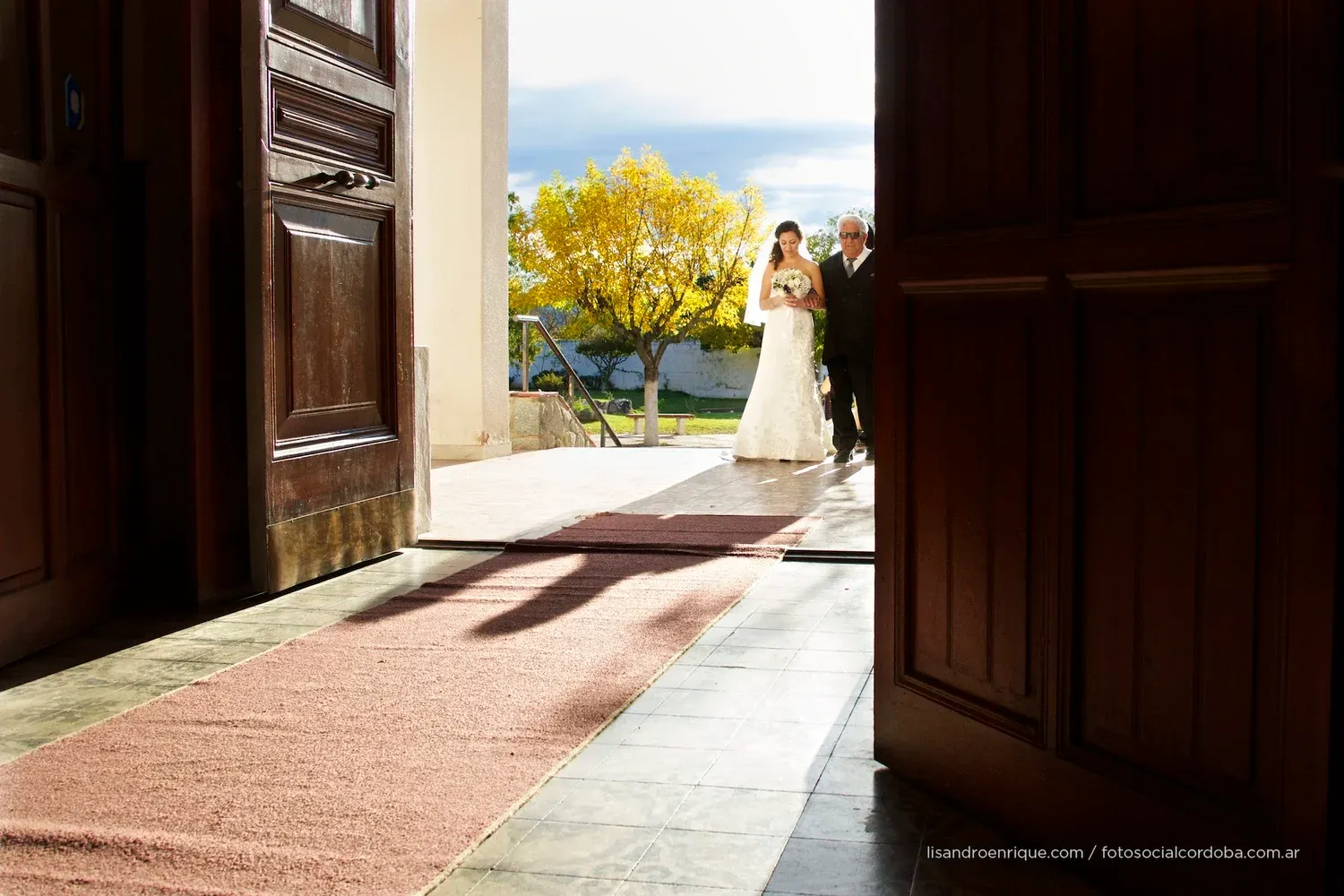 Novia entrando a la iglesia de la mano de su abuelo con la luz de fondo.