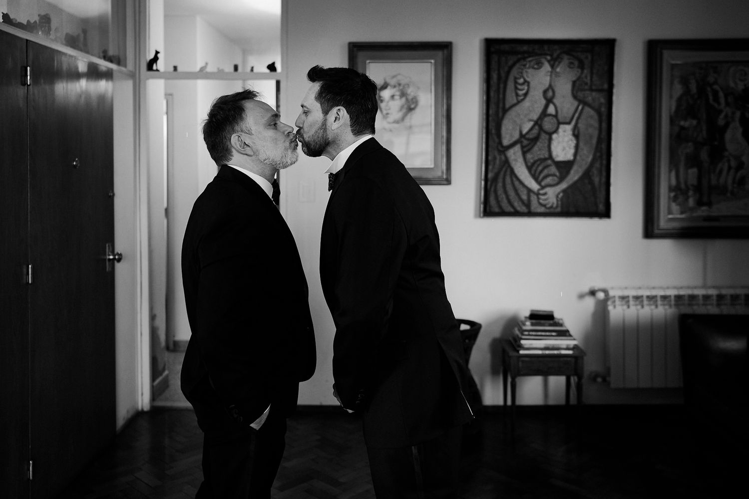 Foto en blanco y negro de dos novios besándose frente a cuadros en la sala de su casa