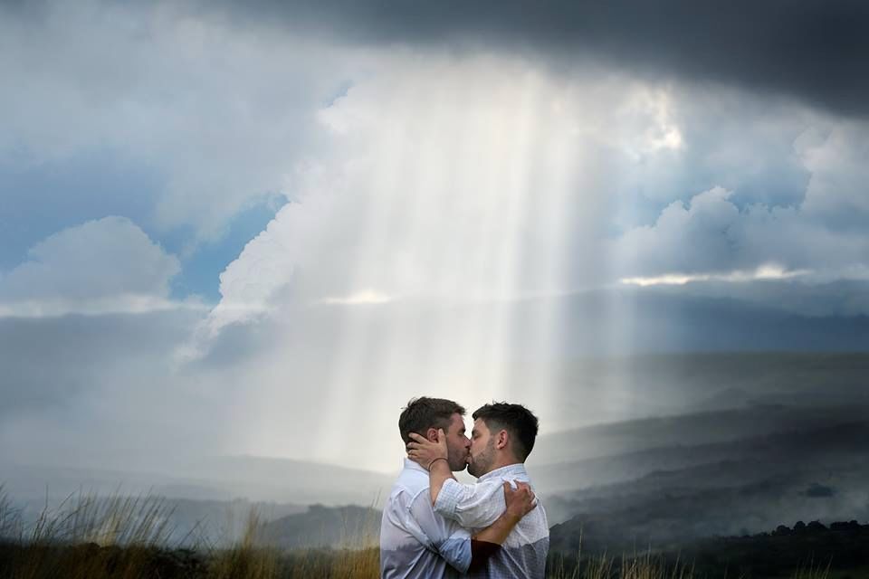 Pareja de novios besándose al aire libre bajo un cielo dramático con rayos de sol entre las nubes
