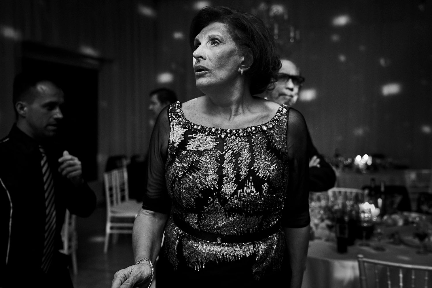 Foto en blanco y negro de una invitada elegante con vestido de lentejuelas mirando hacia arriba durante la fiesta
