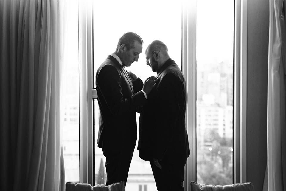Foto en blanco y negro de dos novios abrazados en silueta frente a una ventana con vista a la ciudad