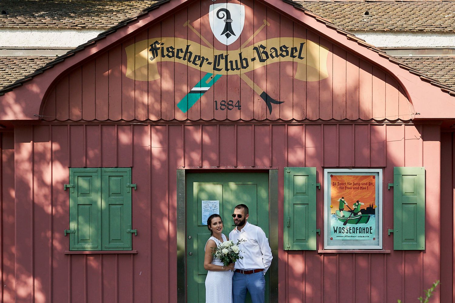 Novios posando frente a la fachada de un antiguo club de remo llamado Fischer-Club-Basel