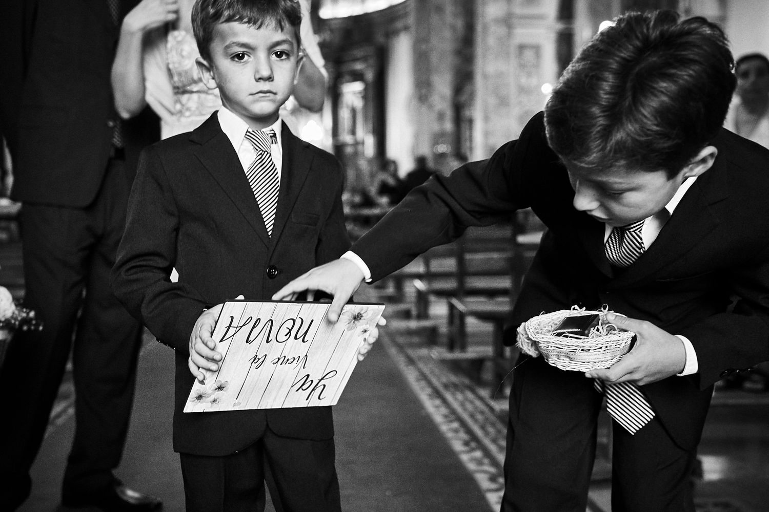 Foto en blanco y negro de dos niños vestidos de traje en la iglesia, uno sostiene un cartel de 
