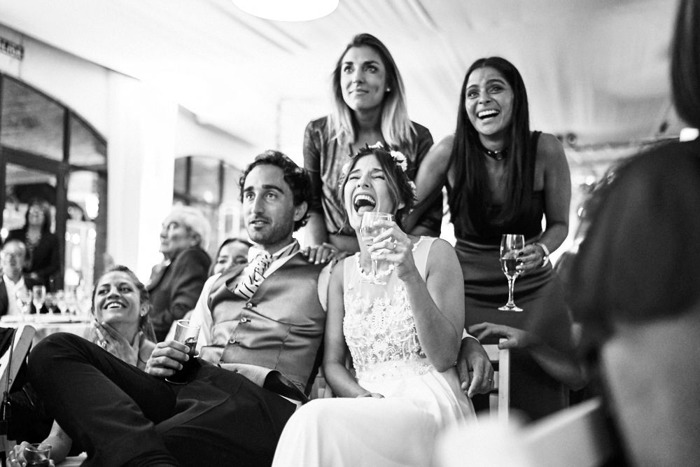 Foto en blanco y negro de los novios y sus amigos riendo a carcajadas durante un brindis