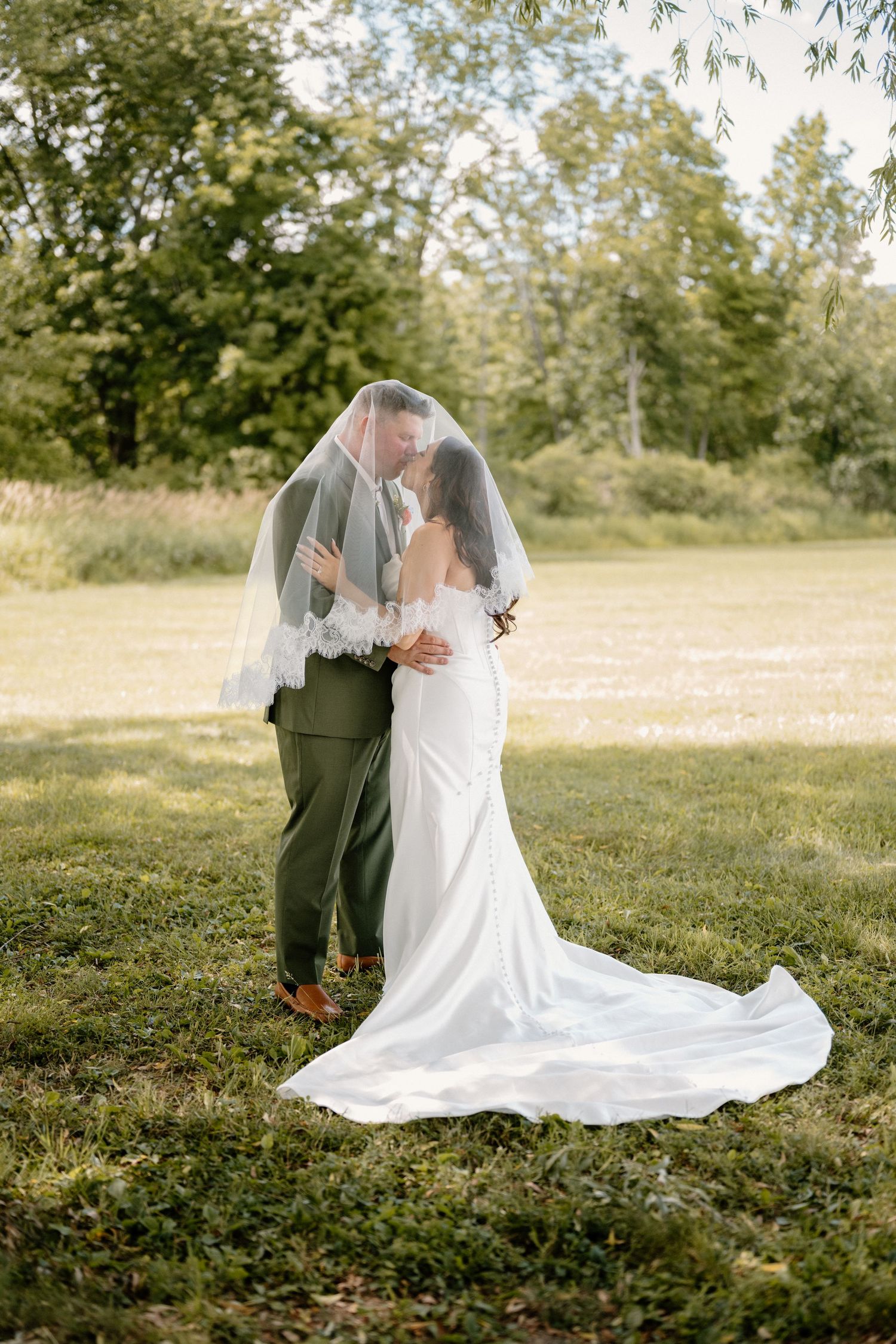 Bride and groom share a romantic moment under a flowing veil in a lush green outdoor setting. Taken in Wallkill, New York