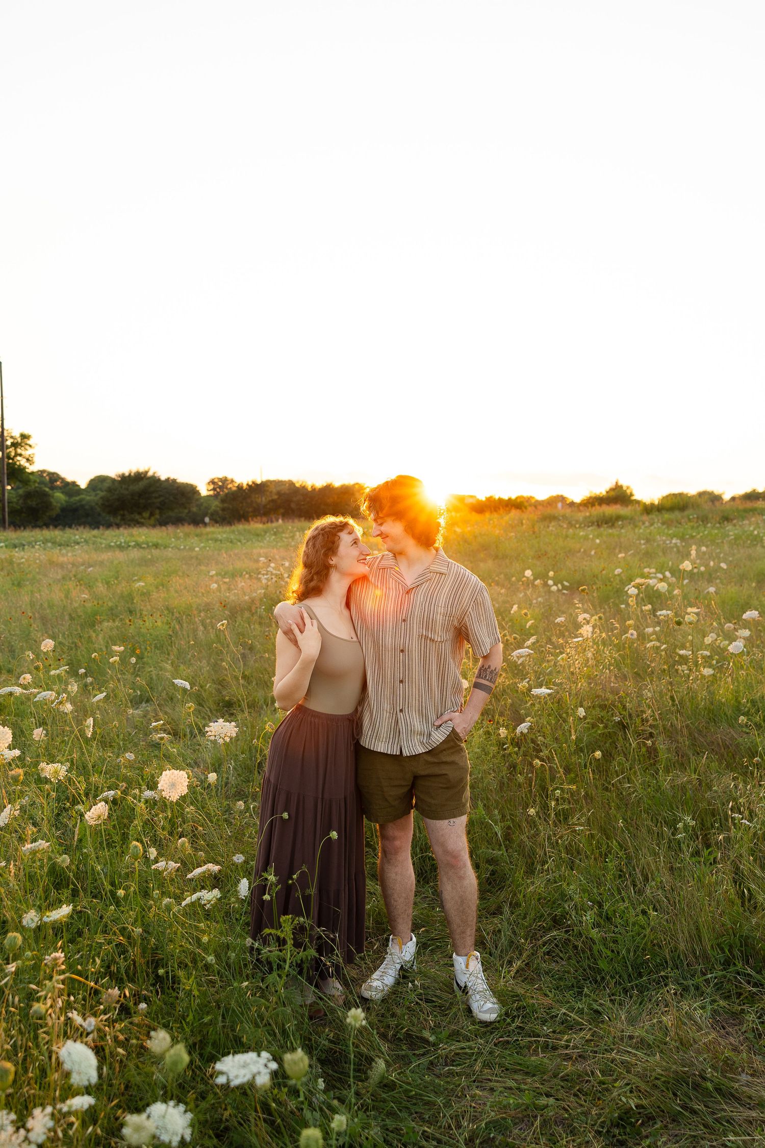 Couple in a field of flowers at sunset in earth toned outfits.
