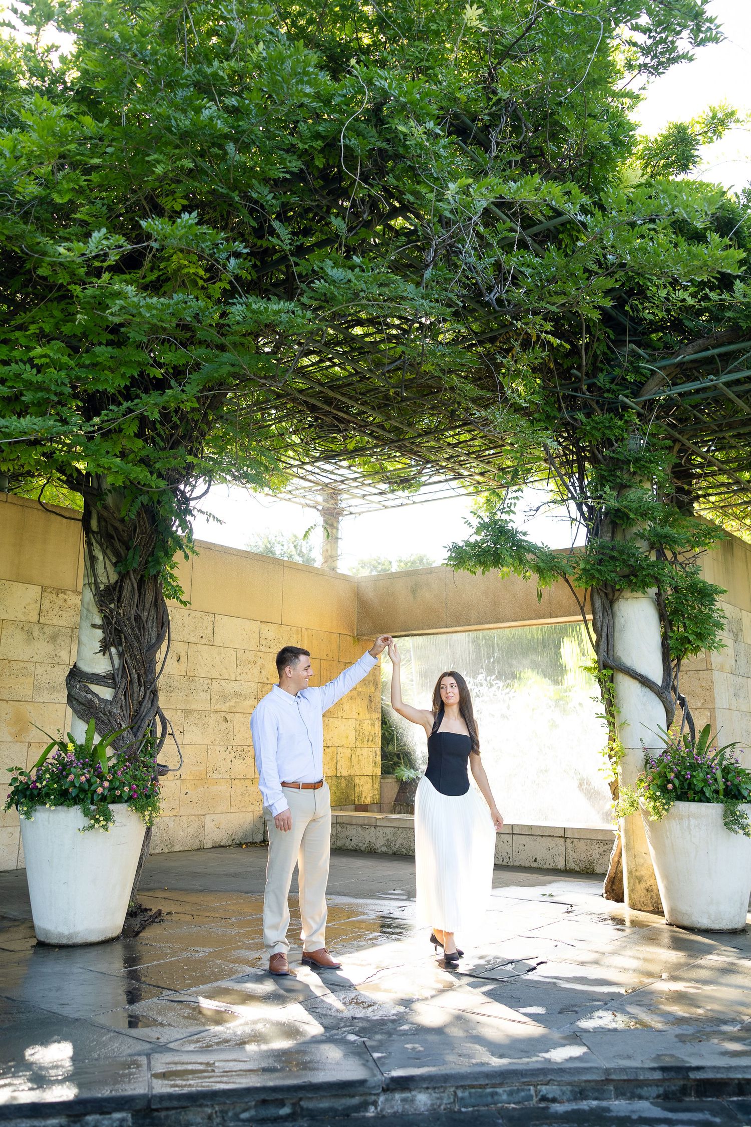 Couple dancing in front of a waterfall in the botanical gardens of Dallas for their engagement photoshoot