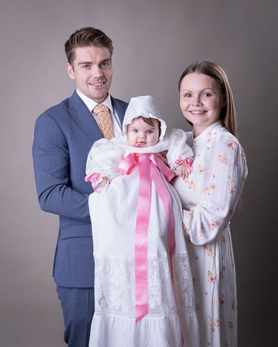 Family portrait with matching white outfits and pink accents against grey studio backdrop.