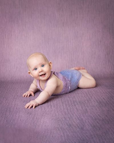 Baby på 6 måneder liggende på magen med lilla body på lilla bakgrunn. Baby bilder i studio på Fjerdingby på Romerike