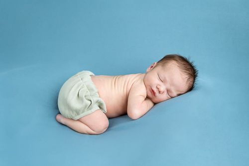 A sleeping newborn baby wearing a diaper lies curled up on a soft blue background.