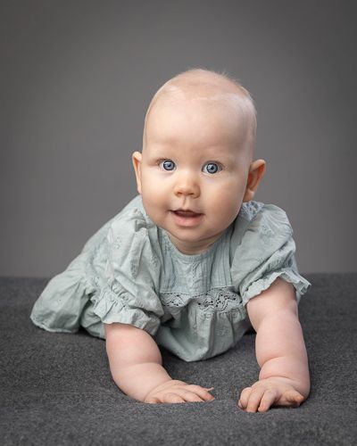 A baby in a sage green ruffled dress crawls on a dark surface in a progression of four sequential photos.