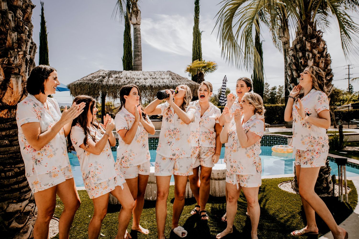 Bridal party in matching floral outfits celebrate outdoors by swimming pool.