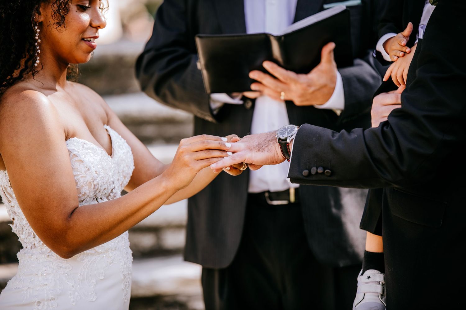 Close-up shot of wedding ceremony ring exchange with detailed view of bride's lace dress.