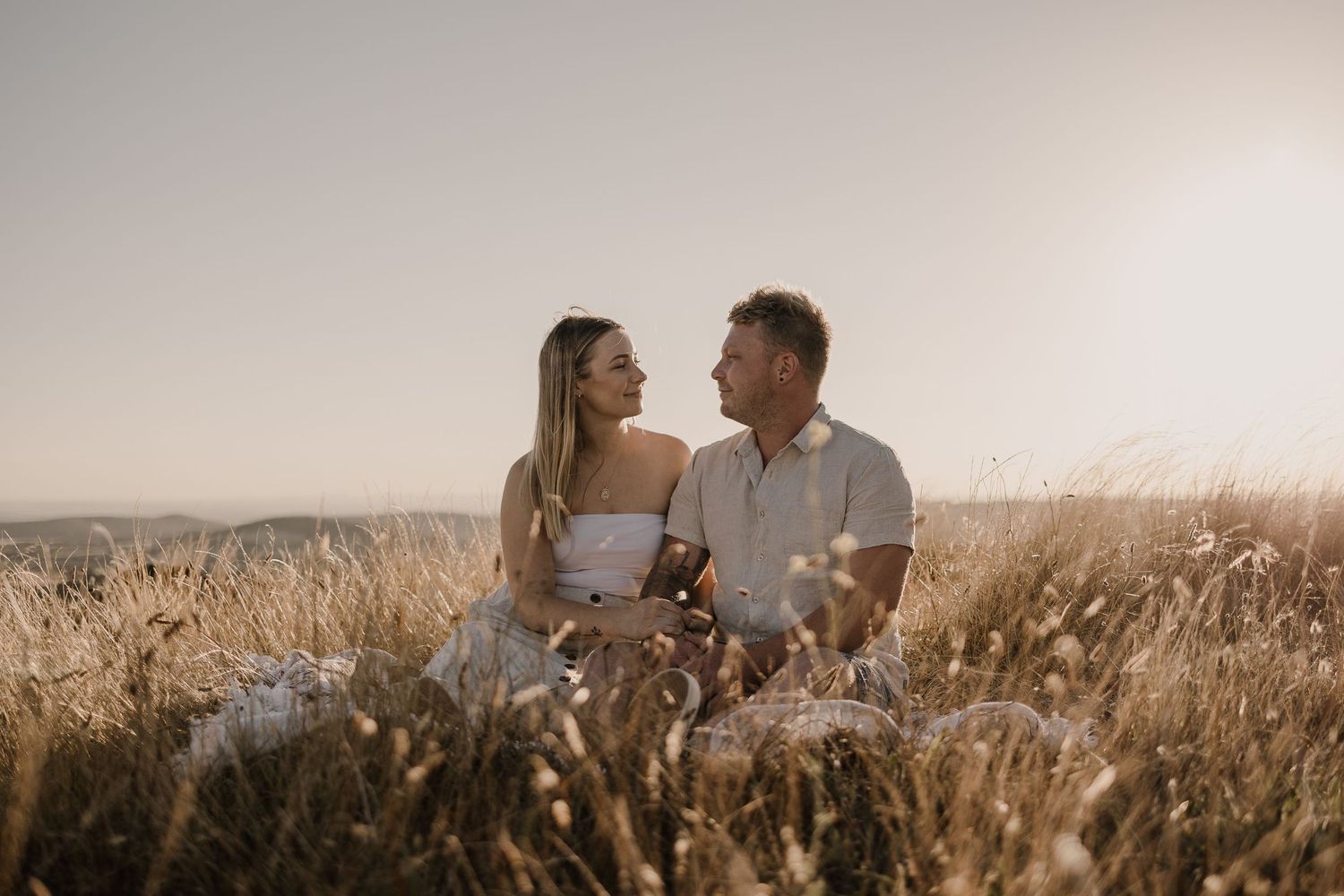 Romantic couple shares tender moments in golden wheat field during sunset.