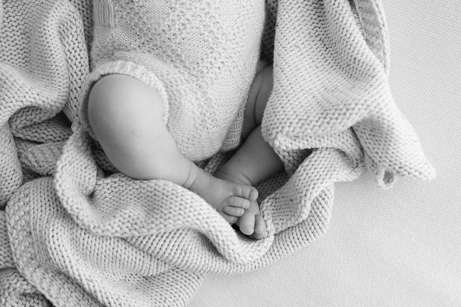 Close-up of tiny baby feet peeking out from a textured white knit blanket.