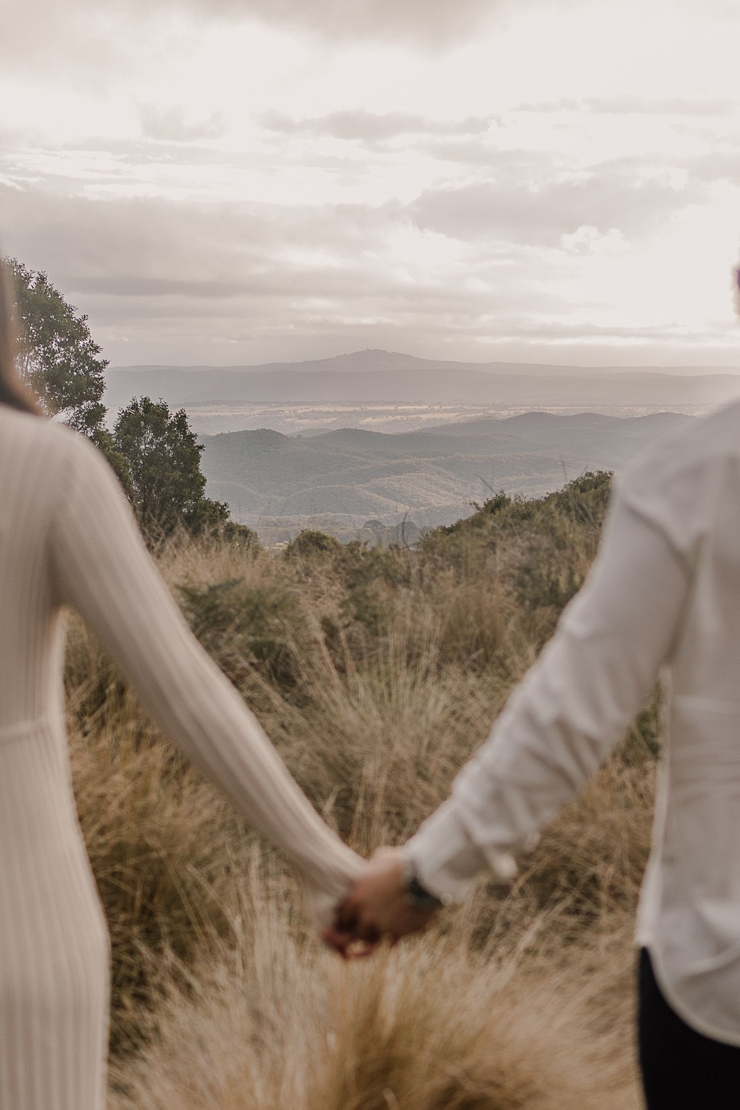 Two people holding hands while overlooking a misty mountain landscape at sunset.