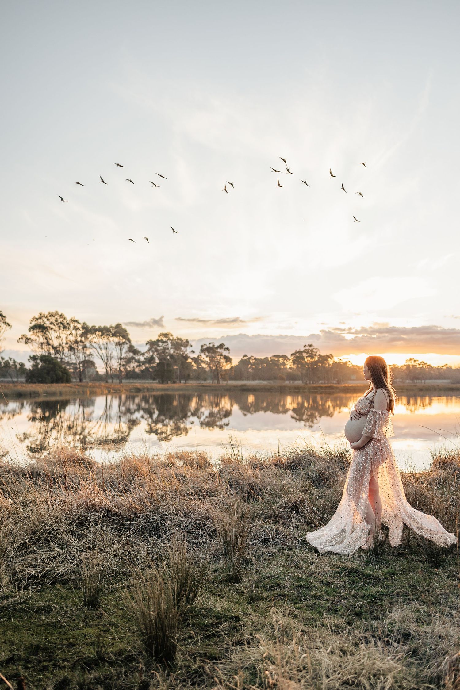 A dreamy sunset photoshoot in a misty field with birds flying overhead and golden light illuminating the natural landscape.