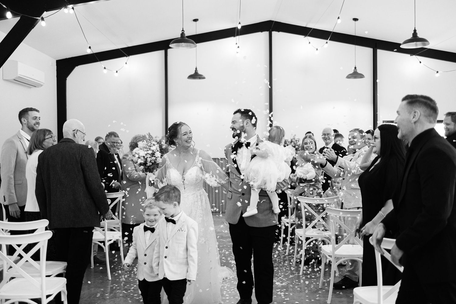 Wedding guests dance and celebrate during a reception in an elegant white tent venue with string lights overhead.
