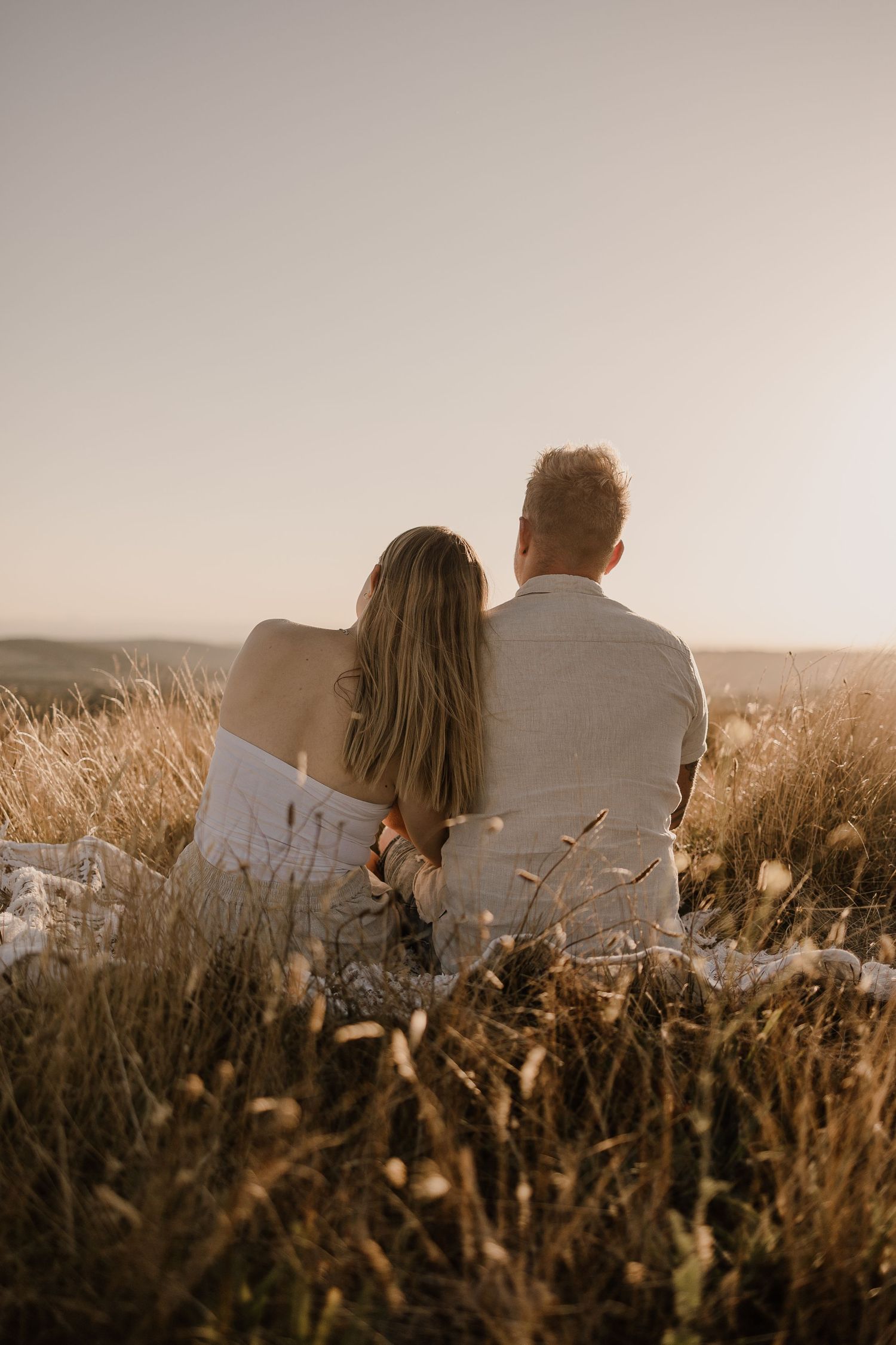 Couple sitting together watching sunset in golden field.