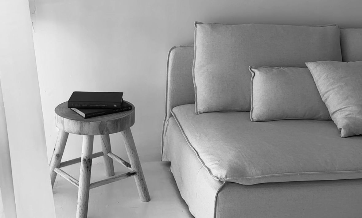 Minimalist black and white interior with a gray upholstered sofa and wooden stool with a coffee mug.