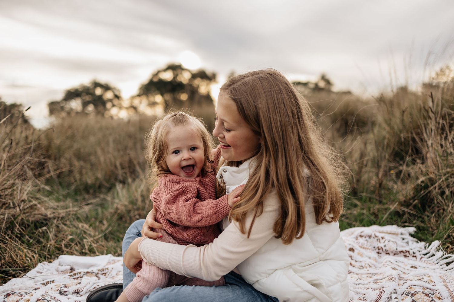Mother and child share tender moment while sitting on blanket in outdoor field setting.