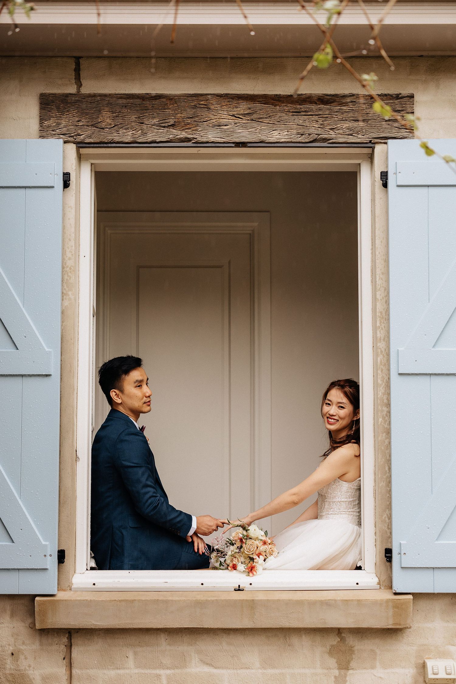 Creative wedding portrait of couple sitting in vintage window frame with white shutters.